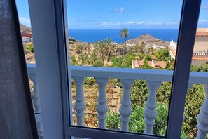 Een balkon met uitzicht op een kustlandschap, inclusief een heuvel en de zee.