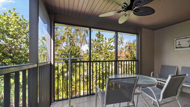 Un balcon avec une table et des chaises, un ventilateur de plafond et une vue sur les palmiers.