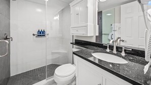 Une salle de bain moderne avec une douche à parois de verre, des toilettes blanches, un lavabo doté d’un plan de travail noir et un grand miroir.