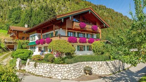 A large, multi-story wooden chalet with balconies, surrounded by lush greenery and a stone wall. - Ferienwohnung "Wilder Kaiser" (Reit im Winkl)