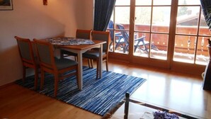 A dining area with a table and chairs, a rug, and a window with curtains. - Ferienwohnung "Wilder Kaiser" (Reit im Winkl)