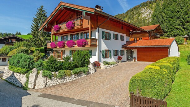 A two-story wooden house with a stone foundation, green shutters, and a red-tiled roof. - Ferienwohnung "Wilder Kaiser" (Reit im Winkl)