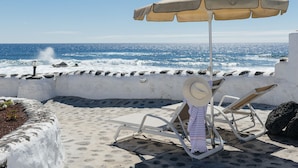 A beachside lounge with a view of the ocean, a sun umbrella, and lounge chairs.