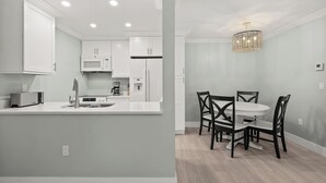 A modern kitchen with white cabinetry, a microwave, and a coffee maker. There is a dining area with a round table and four chairs. - Newly Renovated Partial Beach View 1 bed, 1 bath at Sanibel Moorings #131 (Sanibel)