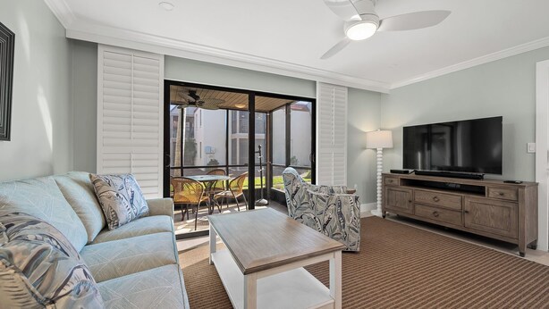 A living room with a sofa, coffee table, TV, and a ceiling fan. - Newly Renovated Partial Beach View 1 bed, 1 bath at Sanibel Moorings #131 (Sanibel)