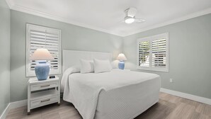 A bedroom with a large bed, two bedside tables with lamps, a ceiling fan, and windows with blinds. - Newly Renovated Partial Beach View 1 bed, 1 bath at Sanibel Moorings #131 (Sanibel)