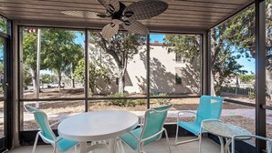 A covered patio with a round table and four chairs, large windows, and a ceiling fan.