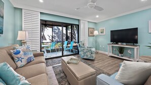 A living room with a sofa, ottoman, and chairs, a television, and a ceiling fan.