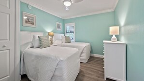 A bedroom with two beds, a ceiling fan, a bedside table with a lamp, and a dresser.
