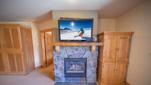 Una sala de estar con chimenea de piedra, armarios de madera y un televisor sobre la chimenea.