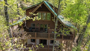 A two-story log cabin with a balcony, surrounded by trees.