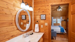 A wooden cabin interior with a bathroom featuring a large mirror, sink, and towel rack. - Air Hockey, Hot Tub. FREE Amenities, Pool, Putt Putt, Fishing, Tennis, etc (Sevierville)