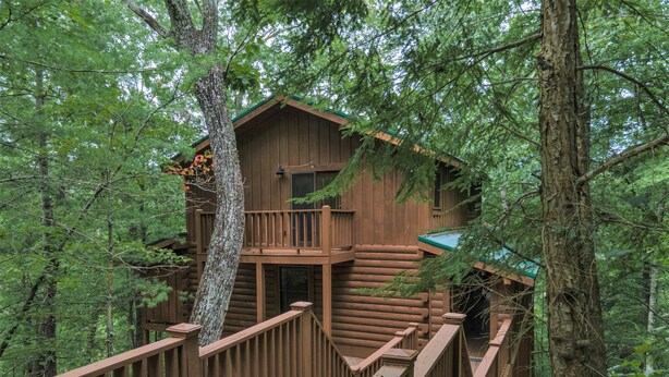 A wooden cabin with a balcony and a staircase leading up to it, surrounded by trees. - Air Hockey, Hot Tub. FREE Amenities, Pool, Putt Putt, Fishing, Tennis, etc (Sevierville)