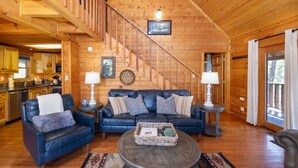 A wooden cabin interior with a living area featuring a sofa set, coffee table, and a staircase. - Air Hockey, Hot Tub. FREE Amenities, Pool, Putt Putt, Fishing, Tennis, etc (Sevierville)