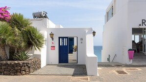 A white building with a blue door, a stone wall with plants, and a view of the sea. - Casa Elena, 3 Bedroom Playa Blanca Sea View (Playa Blanca)