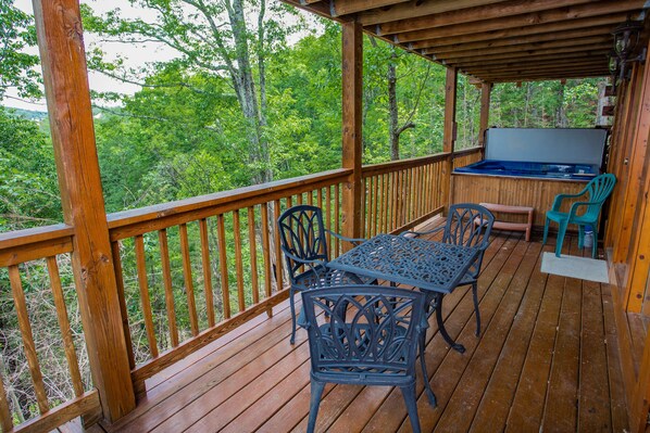 A wooden deck with a table and chairs, a grill, and a view of the forest. - 🌲Abide With Me🏔️ Private Decks, Hot Tub & Game Room (Sevierville)