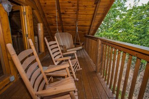 Une véranda en bois avec une chaise suspendue et un banc en bois.