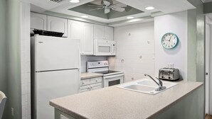 A kitchen with white appliances, a granite countertop, a wall clock, and a ceiling fan.