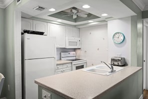 Cozinha com eletrodomésticos brancos, bancada de granito, relógio na parede e ventilador de teto.