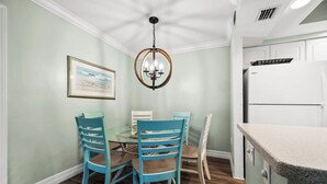 A dining area with a round table, four chairs, a chandelier, and a refrigerator.