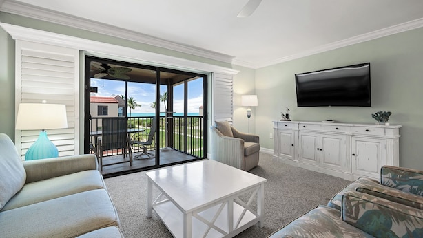 A living room with a sofa, a coffee table, a TV, and a balcony with a view.