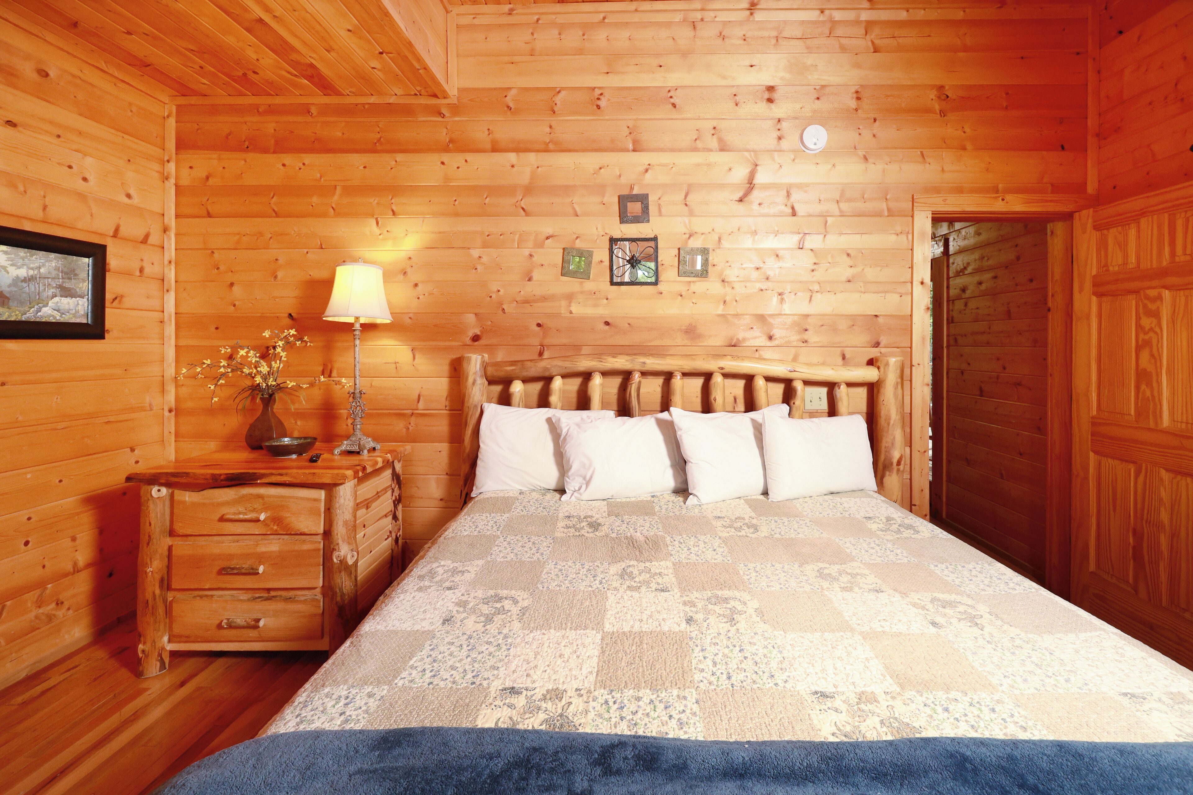 Een slaapkamer in een houten chalet met een bed, een nachtkastje, een lamp en een kleine tafel met een vaas.
