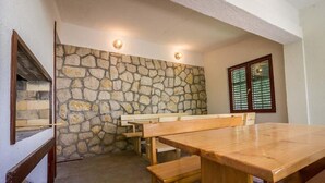 Un mur en pierre avec un banc et une table en bois, une fenêtre avec des stores et une cheminée en pierre.