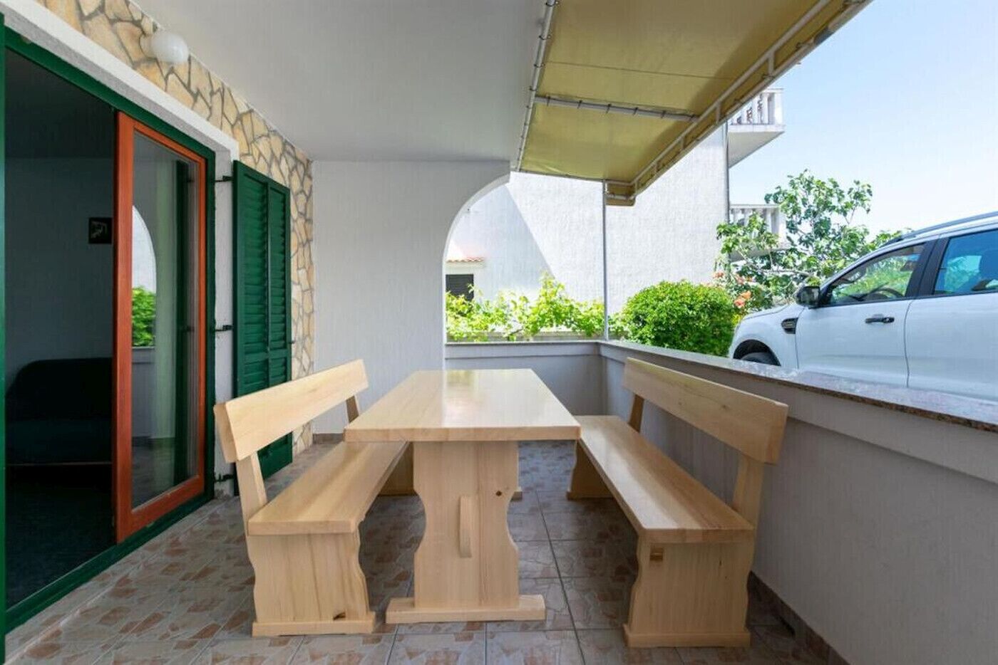 Une table en bois avec des bancs, sur un balcon, et une voiture garée à proximité.