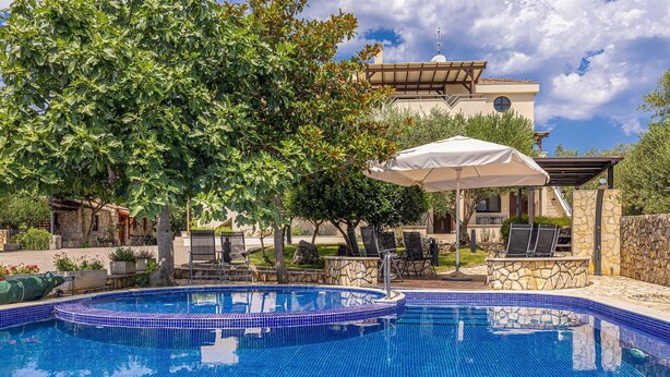 A swimming pool with a tiled edge, surrounded by lounge chairs and an umbrella.