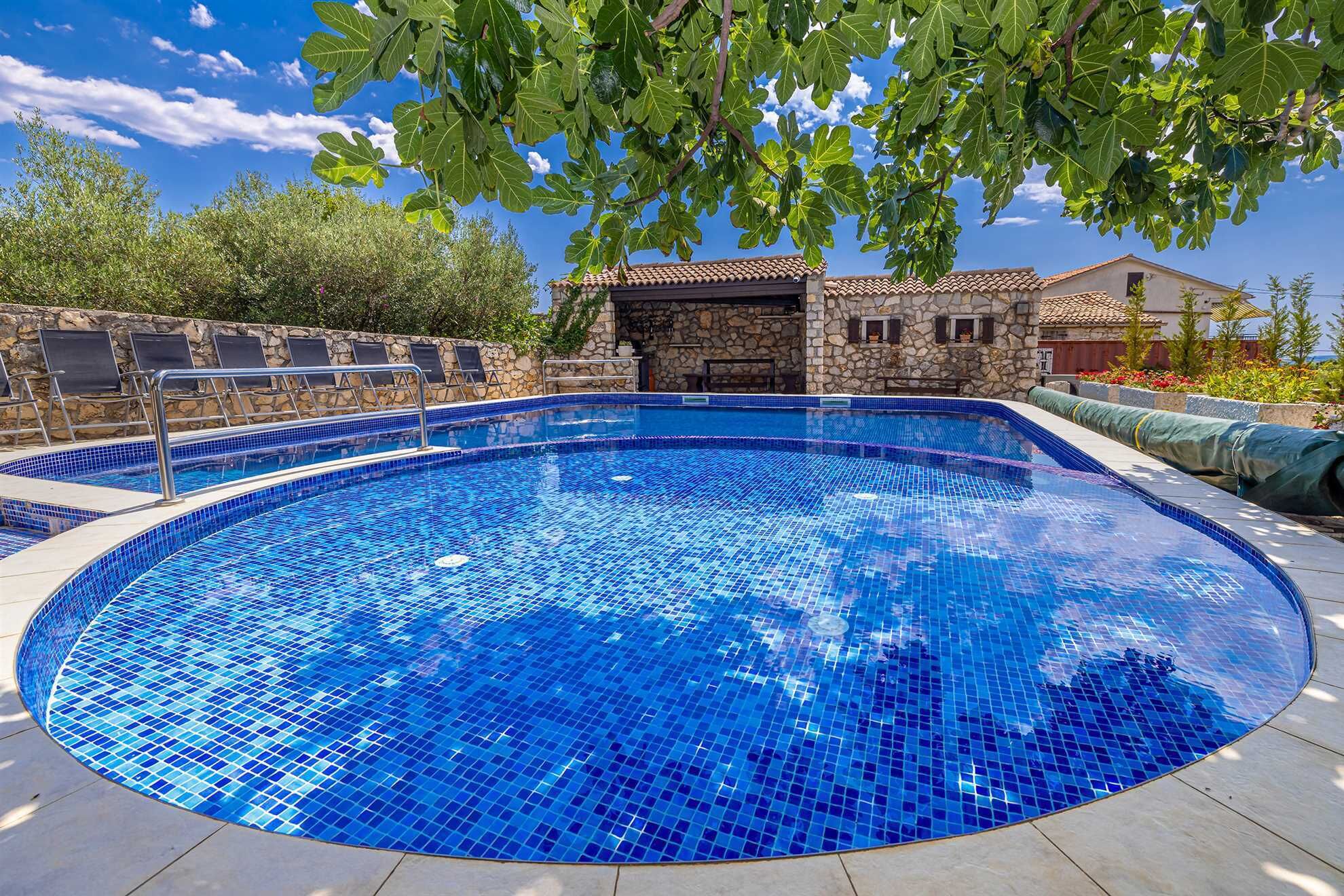 Une piscine circulaire aux carreaux de mosaïque bleus, entourée de murs en pierre et d’un bâtiment en pierre doté d’un toit en tuiles.