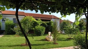 A well-maintained garden with a paved walkway, a stone sculpture, and a building with a red-tiled roof. - Holiday Home in Poreč with Terrace, Air condition, WIFI, Dishwasher (4400-1) (Porec)