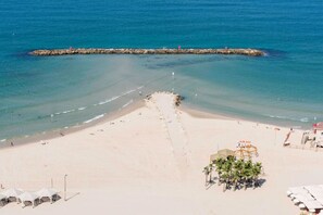 A beach with clear water, a rocky breakwater, and a lifeguard tower.