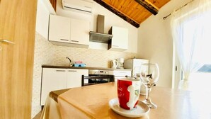 A small kitchen with white cabinets, a wooden ceiling, and a dining table with a red mug and a wine glass. - Apartment in Supetarska Draga with Seaview, Balcony, Air condition, WIFI (4325-2) (Supetarska Draga)