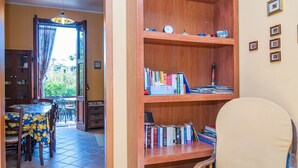 Una habitación con una estantería de madera, una zona de comedor con mesa y sillas, y vistas al exterior a través de una ventana.
