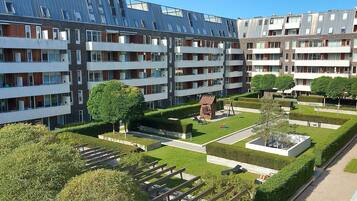 A modern apartment building with multiple balconies, a courtyard with benches, and neatly trimmed hedges.