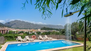 En swimmingpool med liggestole og et vandfald, omgivet af grøn vegetation og et bjergrigt landskab.