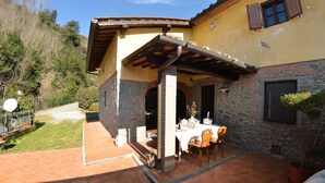 Un patio con mesa lista para comer, paredes de piedra y vista a un cerro cubierto de bosque.