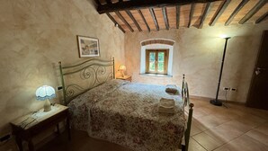 Un dormitorio con una cama, una mesita de noche, una lámpara, una ventana y una puerta.