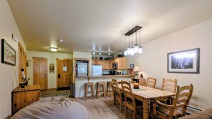 Eine kompakte Küche mit Holzschränken, einem Kühlschrank und einer Mikrowelle. Es gibt eine Essecke mit Tisch und Stühlen sowie einen großen Sitzsack.