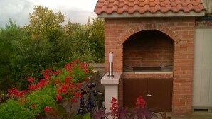 Un horno de ladrillo al aire libre con chimenea, rodeado de macetas con plantas y flores.