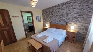 Une chambre à coucher avec un lit en bois, des tables de chevet, un banc, un mur en pierre et une porte en bois.