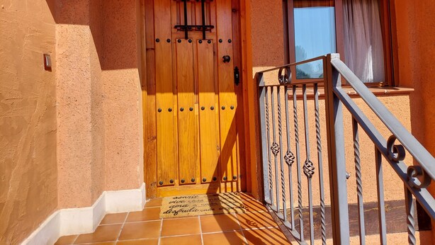 Une porte en bois avec un portail en métal, une fenêtre avec des rideaux et un sol carrelé menant à un balcon.