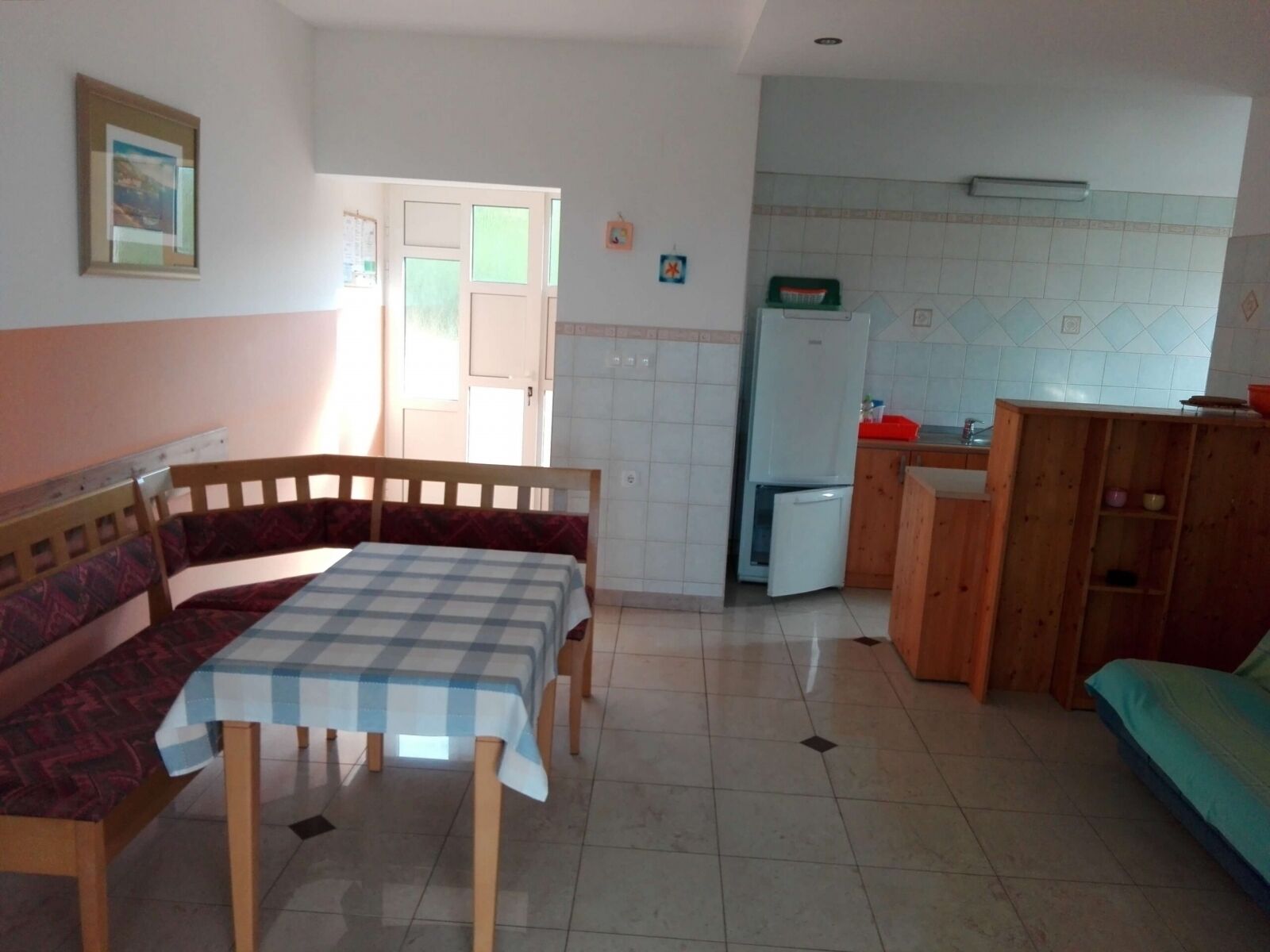 A compact kitchen with a dining table and bench, a refrigerator, and a wooden cabinet.