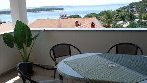 Un balcón con mesa y sillas, con vistas a la costa, edificios y vegetación.