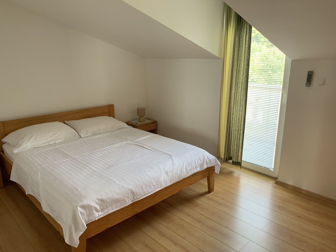 A bedroom with a wooden bed, a nightstand, a lamp, and a window with curtains.