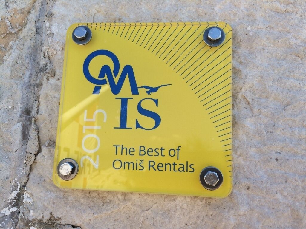 A yellow plaque with the text 'OMiš 2015 The Best of Omiš Rentals' mounted on a stone wall.