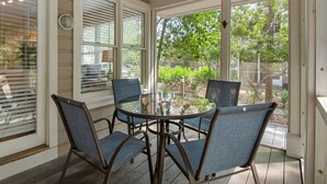 Une terrasse couverte avec une table et des chaises en verre, de grandes fenêtres et un ventilateur de plafond.