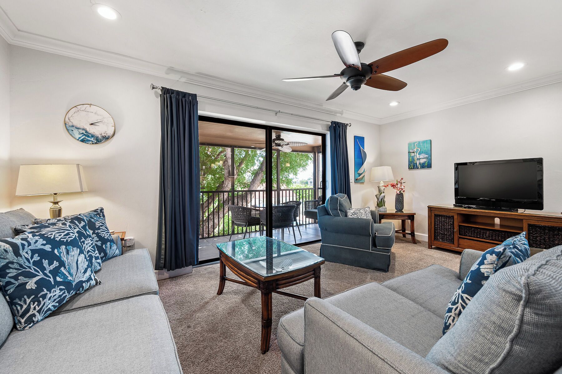 A living room with a ceiling fan, a TV, and a balcony with outdoor furniture.