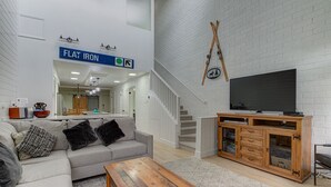A modern living room with a grey sofa, a wooden coffee table, and a TV on a wooden cabinet. A staircase leads to an upper level. - Captain Molly 3 Bedroom Condo, Centrally Located in PC, Mins to Skiing! (Park City)