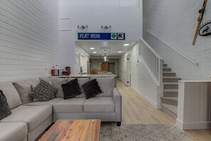 A modern living room with a sofa, coffee table, and a staircase. A sign above indicates a direction to 'Flat Iron'.
